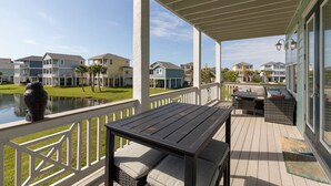 A covered deck with a table and seating, overlooking a body of water and houses. - Beautiful Pointe West Beach House w/Great Sunsets, Beach, Bay Views & Pet Ok (Galveston)