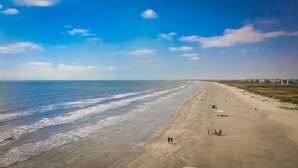 A wide beach with gentle waves, a clear sky, and a few people walking. - Beautiful Pointe West Beach House w/Great Sunsets, Beach, Bay Views & Pet Ok (Galveston)