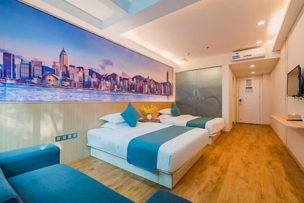 A hotel room with a bed, two bedside tables, a chair, a painting of a city skyline, and a wooden floor.