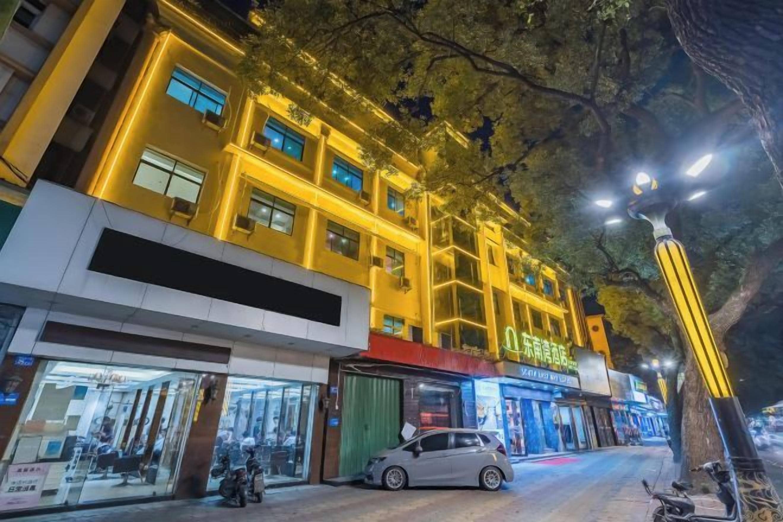 Un edificio de varios pisos con ventanas iluminadas y un árbol en la fachada.