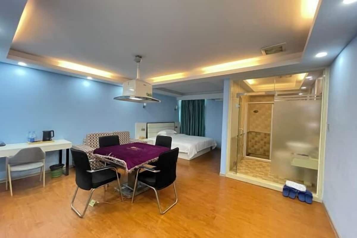 A compact hotel room with a bed, a small table with chairs, a desk, and a shower area.