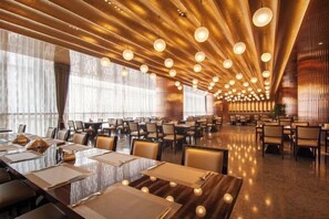 A spacious dining area with long tables and chairs, warm lighting, and large windows. - South East Bay Hotel (Huizhou West Lake Pedestrian Street) (Huizhou)