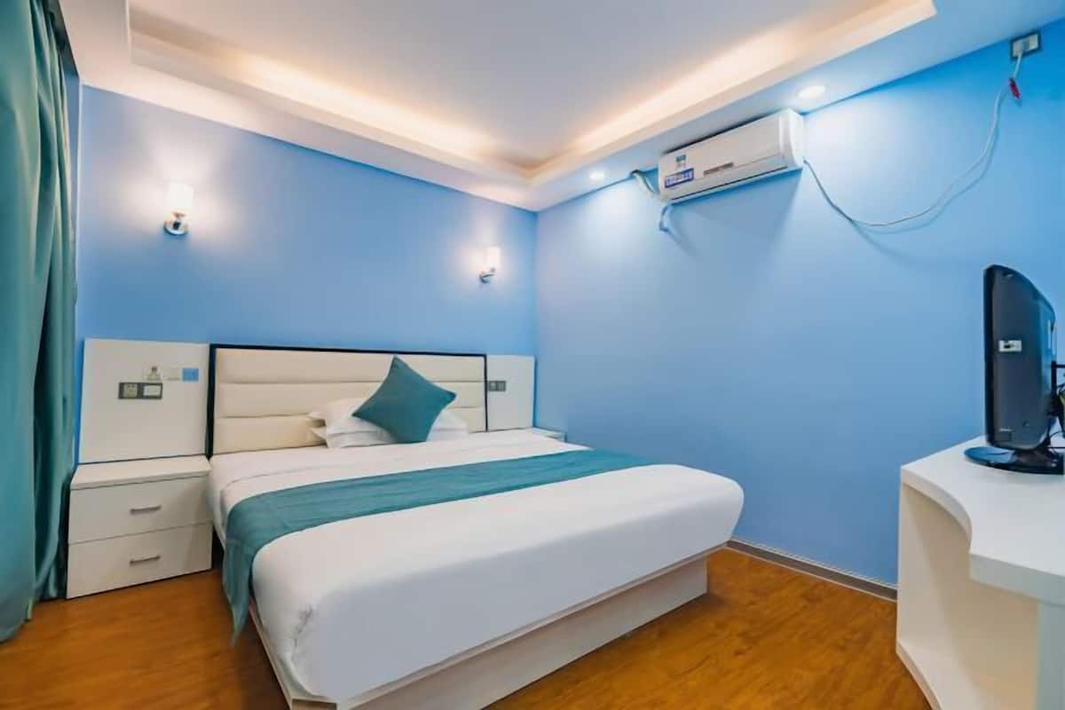 A hotel room with a bed, bedside tables, an air conditioning unit, and a desk with a computer.