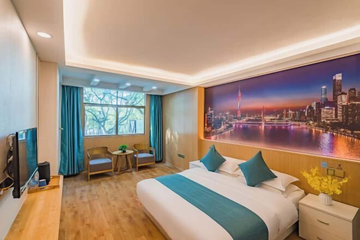 A hotel room with a large bed, a desk, a chair, a TV, and a cityscape painting on the wall.