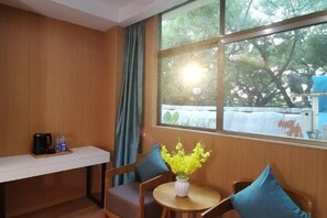 Et værelse med trævæg, et vindue med udsigt til træer, et lille bord med en vase blomster og en stol med pude.