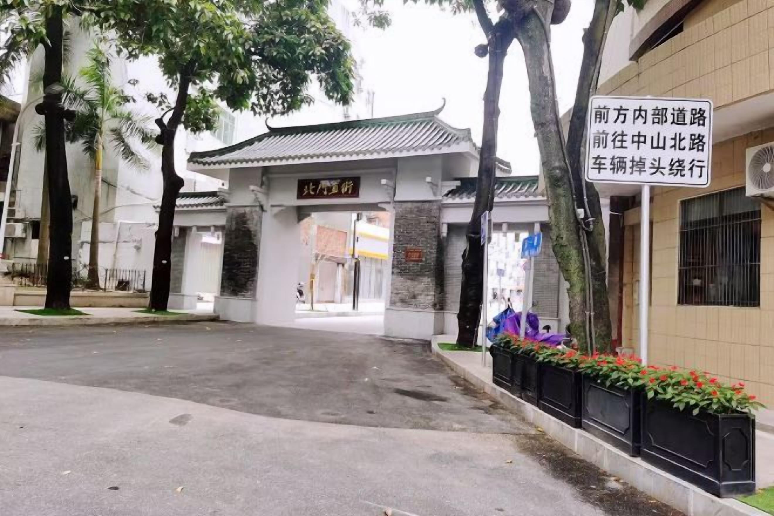 A traditional Chinese gate with a sign, a paved entrance, and a building with a tiled roof.