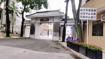 A traditional Chinese gate with a sign, a paved entrance, and a building with a tiled roof.