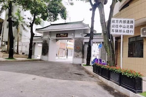 Une porte chinoise traditionnelle, agrémentée d’une enseigne, avec une allée dallée et un bâtiment doté d’un toit en tuiles.