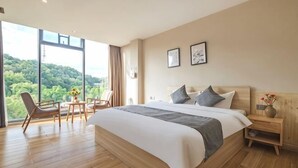 Ein Schlafzimmer mit einem großen Bett, einem Schreibtisch mit Stühlen, einem Nachttisch und Blick auf Grünflächen.