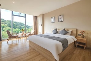 Un dormitorio con una cama grande, un escritorio con sillas, una mesita de noche y vistas a zonas verdes.