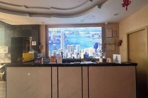 Un espace d’accueil avec vue sur la ville à travers une grande fenêtre, un comptoir d’accueil et une porte sur la droite.