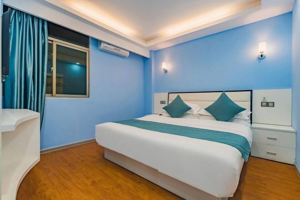 A bedroom with a bed, bedside tables, an air conditioning unit, and a window with curtains.