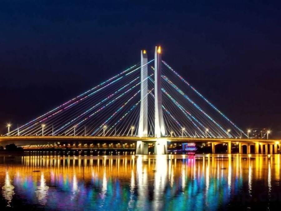 A nighttime view of a cable-stayed bridge with its lights reflecting on the water.