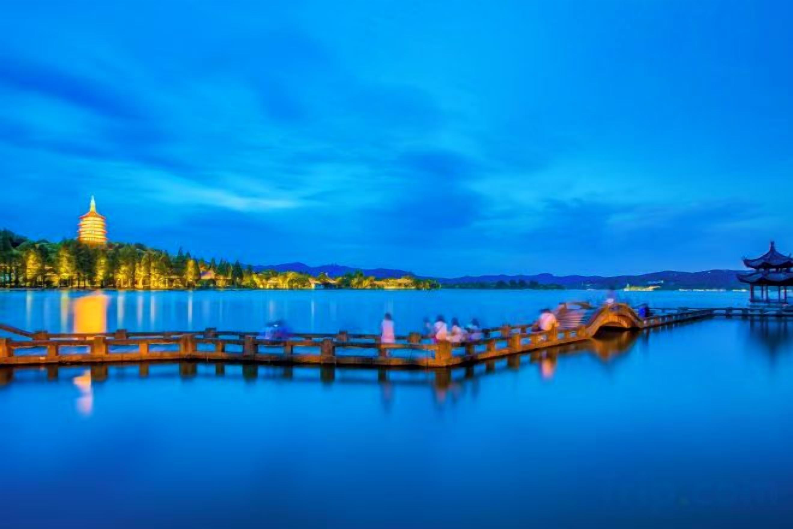 A calm lake with a wooden pier, a pagoda, and a traditional building in the background.