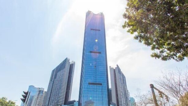 Ein modernes Hochhaus mit Glasfassade, umgeben von weiteren hohen Gebäuden und einer belebten Straße mit Autos und Ampeln.