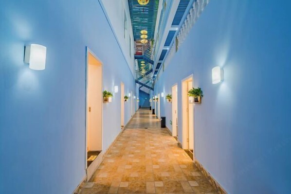 Een hotelgang met blauwe wanden, een betegelde vloer en een centrale trap.