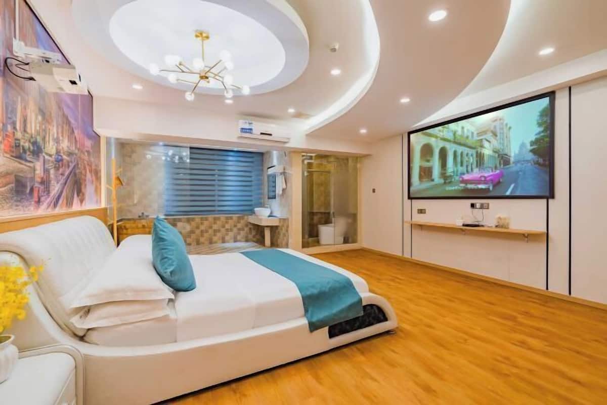 A modern bedroom with a curved ceiling, a large bed, a TV, and a glass shower enclosure.