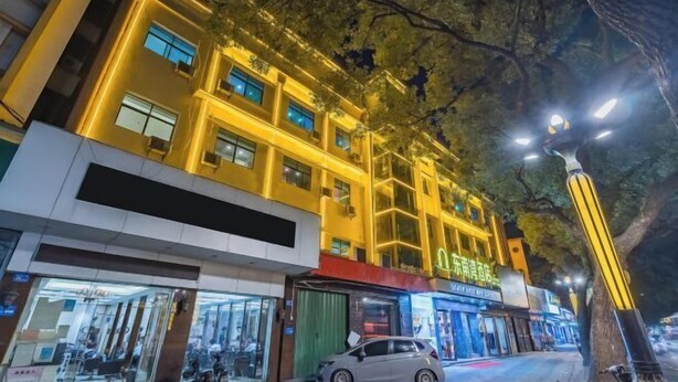 A multi-story building with illuminated windows and signage, a parked car, and a tree in the foreground. - South East Bay Hotel (Huizhou West Lake Pedestrian Street) (Huizhou)