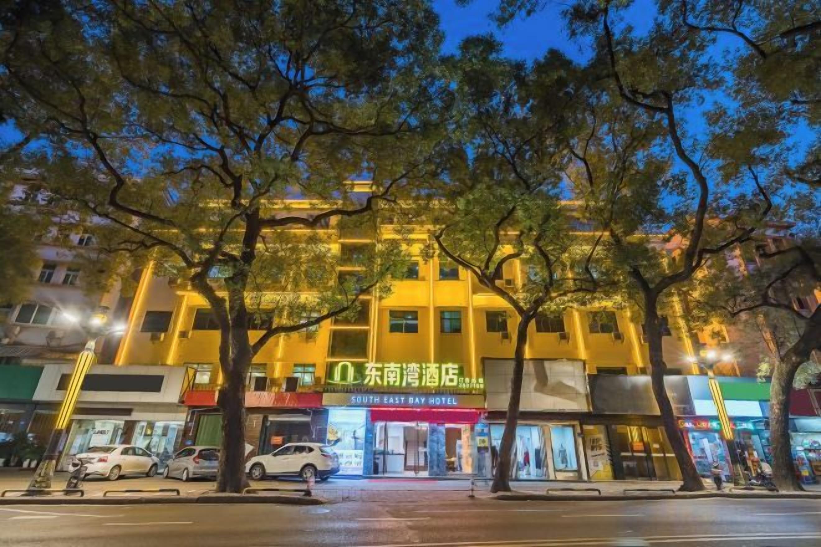 Un hotel con diversi piani, un ingresso ben visibile e vista sulla strada con auto parcheggiate e alberi.