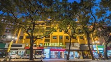 Un hotel con diversi piani, un ingresso ben visibile e vista sulla strada con auto parcheggiate e alberi.