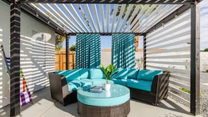 Un espace extérieur aménagé avec un canapé et une table ronde, installé sous une pergola recouverte d’un tissu à rayures.