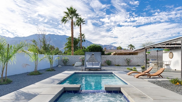 Une piscine rectangulaire agrémentée d’une cascade, entourée d’une terrasse avec des chaises longues et un petit espace salon abrité.