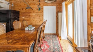 En träinredd interiör med ett matbord, stolar, ett kylskåp och fiskeutrustning på väggen.