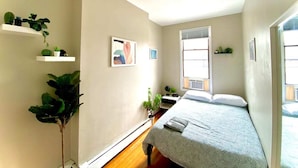Une chambre à coucher comprenant un lit, des tables de chevet, une grande fenêtre et des étagères murales ornées de plantes.
