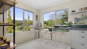 A modern kitchen with large windows, bar stools, and a view of greenery.