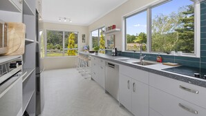 A modern kitchen with large windows, a countertop with a sink, and a dining area with stools.