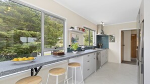 A modern kitchen with a large window, a countertop with stools, and a view of greenery outside.
