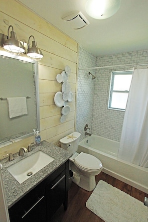 A bathroom with a sink, toilet, and bathtub, wooden paneling, and a window. - Waterfront Retreat with Private Dock on the Sound (Kill Devil Hills)