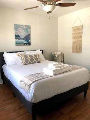 A bedroom with a bed, a ceiling fan, a wall-mounted macrame piece, and a painting of clouds. - Waterfront Retreat with Private Dock on the Sound (Kill Devil Hills)