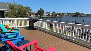 Eine Terrasse mit bunten Adirondack-Stühlen, einem Grill und Blick auf einen See mit Häusern im Hintergrund.