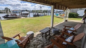 Ein überdachter Außenbereich mit Holzkufen und einem Tisch, mit Blick auf einen Yachthafen und Boote.