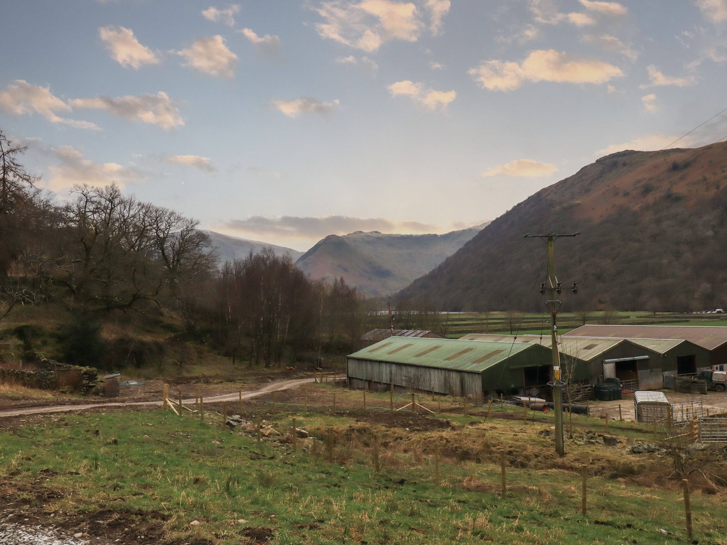 A rural landscape with a dirt road, green fields, and a mountain range in the background.