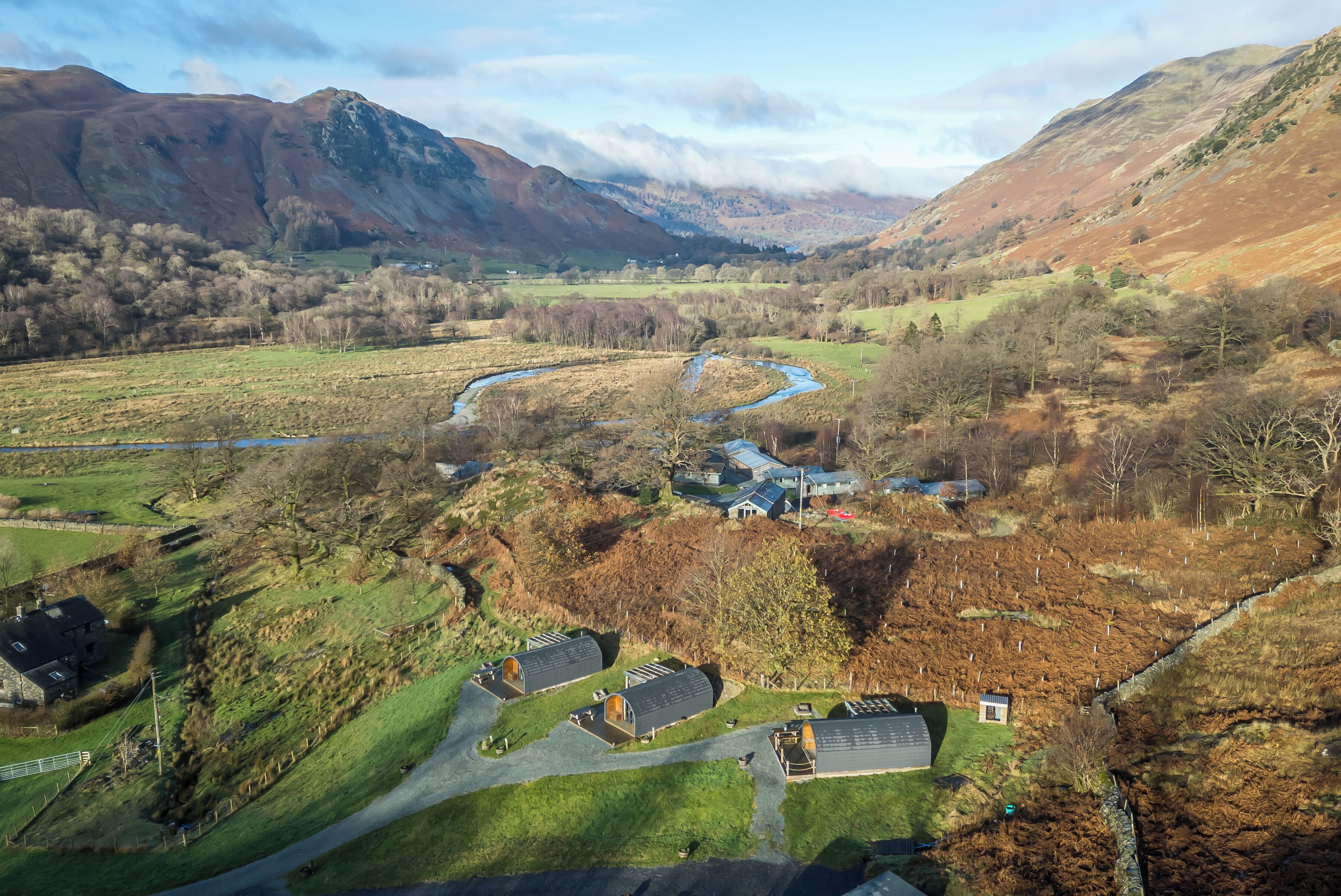 A rural landscape with a winding river, a small cluster of buildings with pitched roofs, and a road leading to them.
