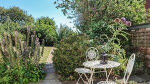 A garden with a metal table and chairs, a pathway, and various plants. - Hops Cottage (Ashbourne)
