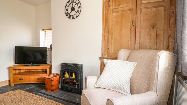 A living room with a television, a fireplace, a clock, and a large wooden wardrobe. - Hops Cottage (Ashbourne)