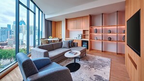 A modern living room with a sofa, chairs, a coffee table, and a TV. There is a kitchen area with cabinets and a dining table. The room has large windows with a city view. - Fairfield by Marriott Chow Kit Kuala Lumpur (Kuala Lumpur)