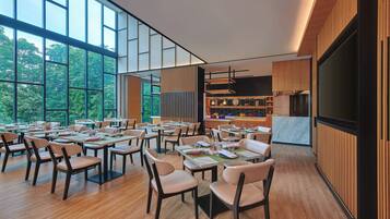 A modern dining area with tables and chairs, large windows, and a kitchen area in the background.