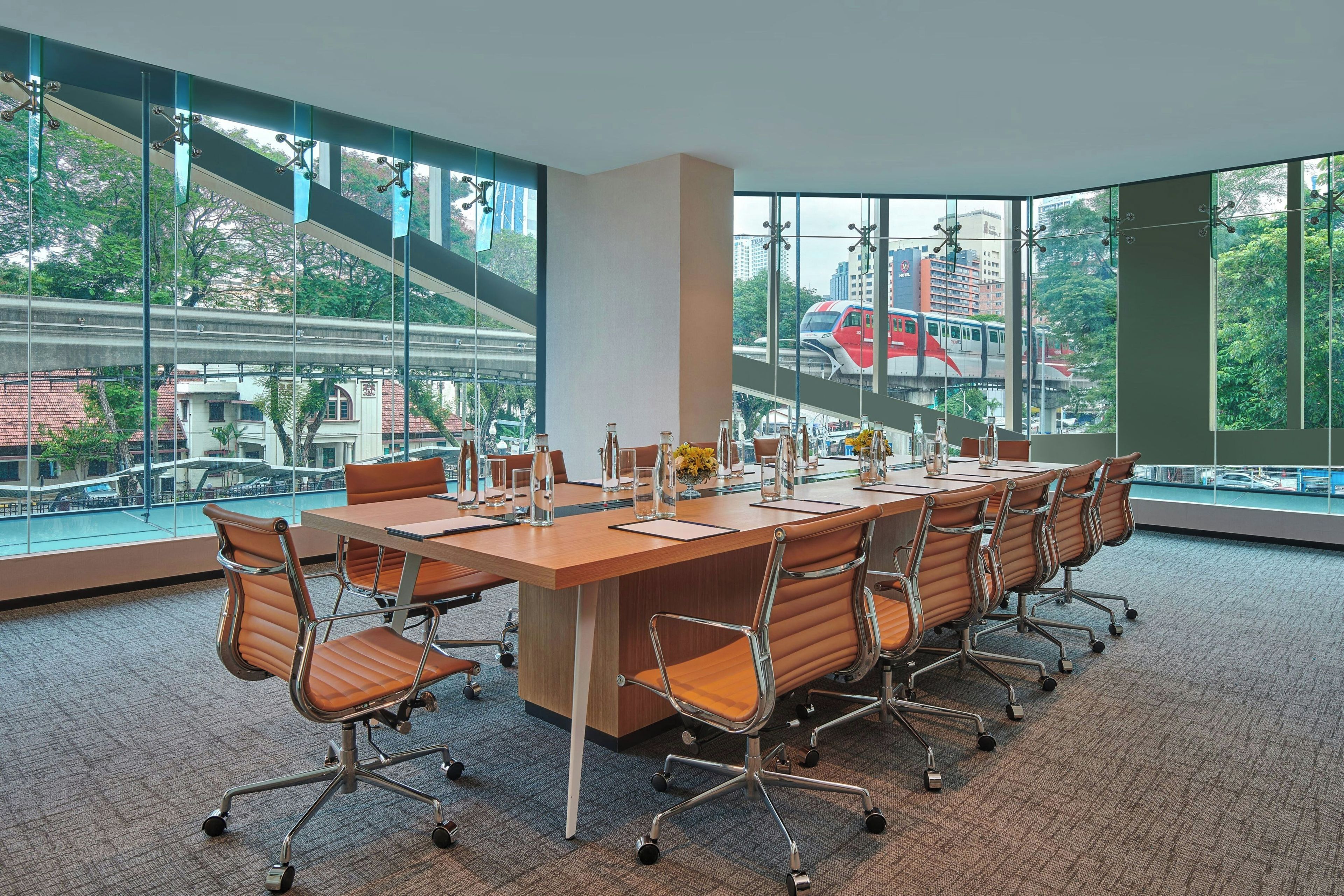 A conference room with a large table, chairs, and a view of a cityscape through large windows.