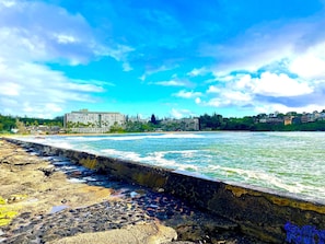 A coastal hotel with a beachfront view, a rocky shoreline, and a clear blue sky.