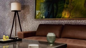 Ein modernes Wohnzimmer mit einem Glastisch, einem braunen Ledersofa, einer Stehlampe und einem großen abstrakten Gemälde an der Wand.