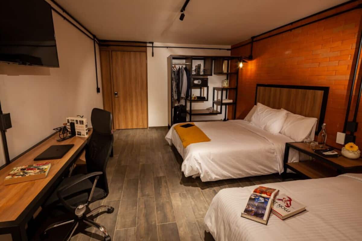 A hotel room with two beds, a desk, a chair, a wardrobe, and a TV.