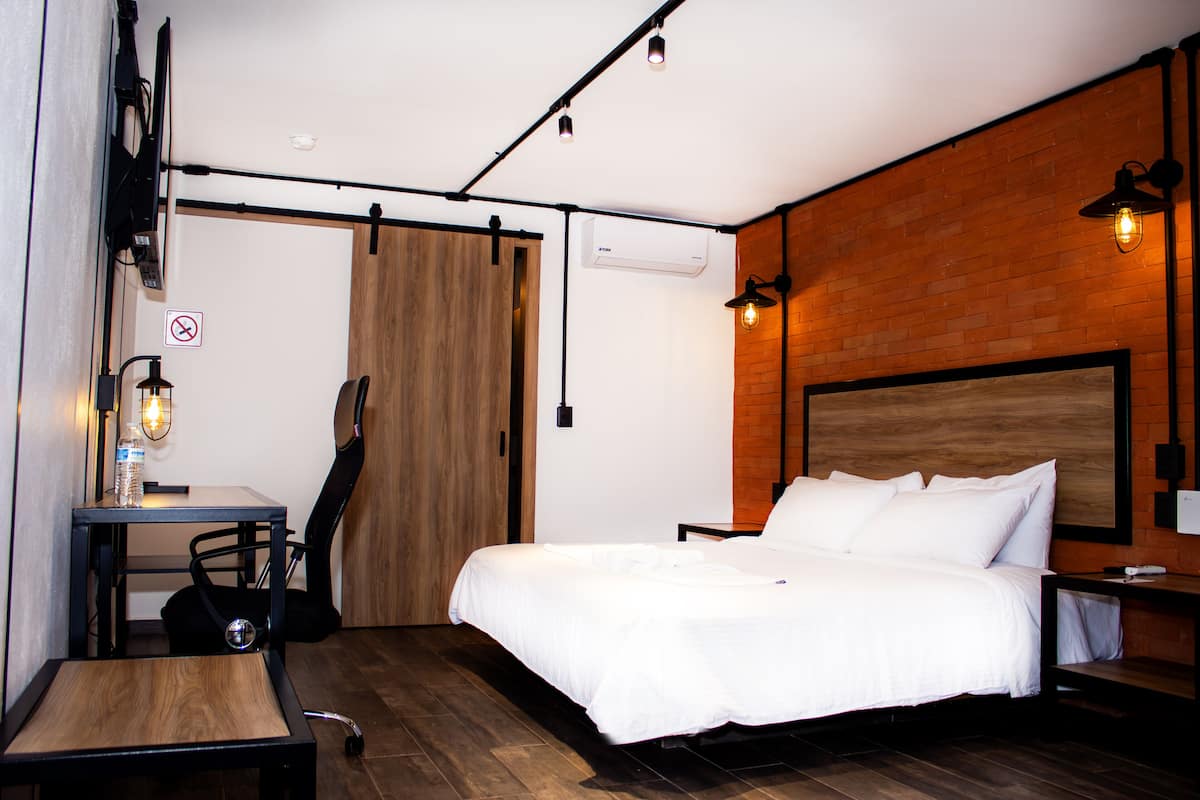 A bedroom with a bed, a desk, a chair, a guitar, and a wooden floor.