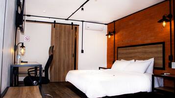 Un dormitorio con una cama, un escritorio, una silla, una guitarra y suelo de madera.