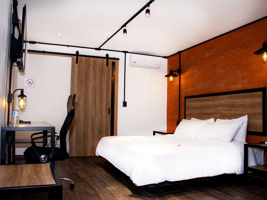A bedroom with a bed, a desk, a chair, a guitar, and a wooden floor.
