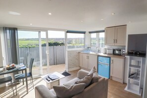 Et moderne køkken med et blå køleskab, et spiseområde med bord og stole, og en stor skydedør, der fører ud til en balkon med udsigt over landskabet.