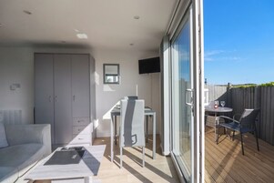 A modern living room with a sofa, a dining table, and chairs. There is a sliding glass door leading to an outdoor patio area with a table and chairs.